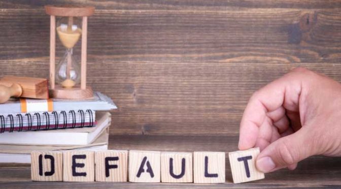 The word defaulted spelt with blocks on a desk, next to an hourglass