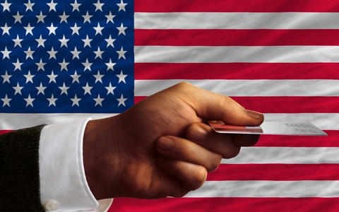 A man holding a credit card in front of an American flag