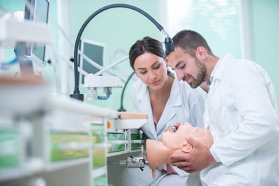 Two dental students working on a prosthetic mouth in dental school