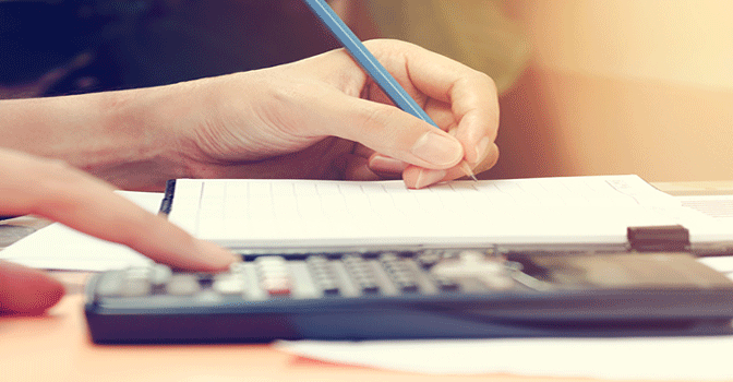 A women at a desk calculating her student loan balance with pen, paper and a calculator.