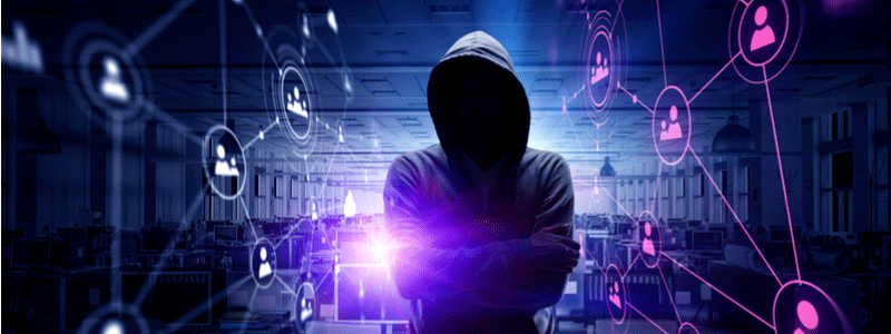 A hooded man in front of a number of computers in the dark web