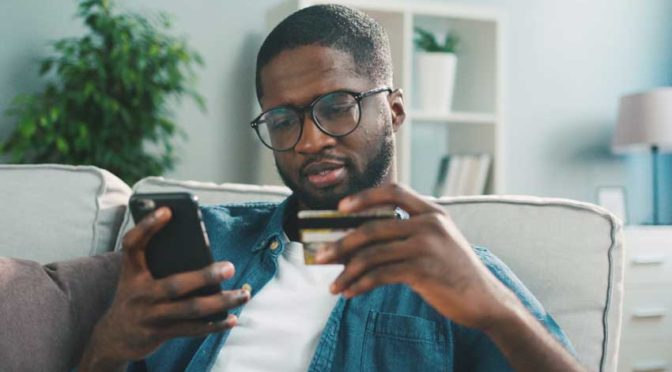 A young man using a credit card and a mobile phone to pay off his student loans