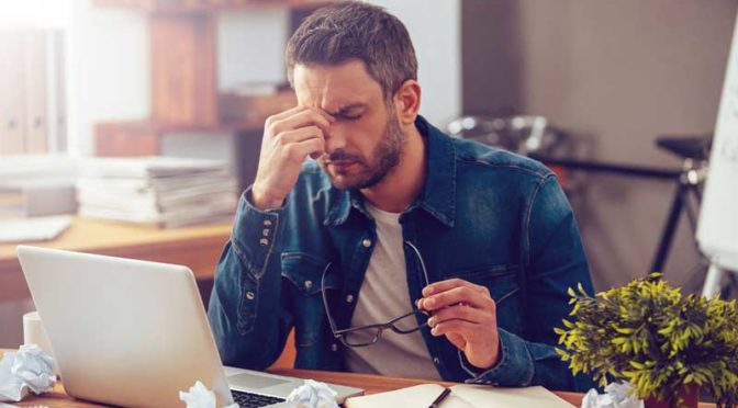 a man at a computer seemingly frustrated at his computer