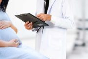 A pregnant woman sitting on a medical table near a doctor gynecologist holding a clipboard