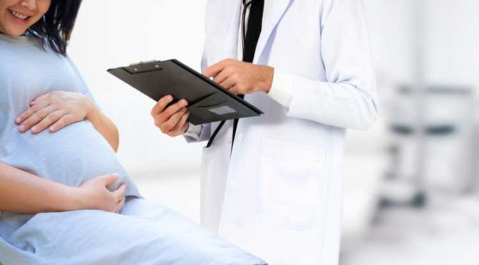 A pregnant woman sitting on a medical table near a doctor gynecologist holding a clipboard