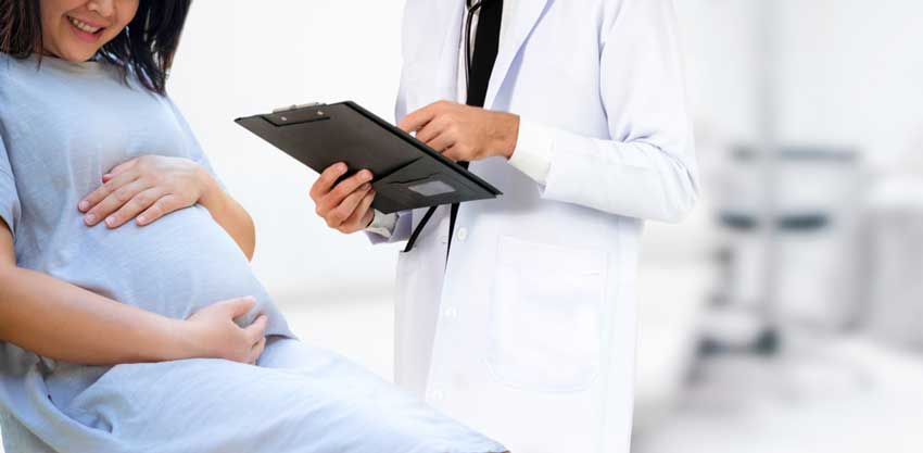 A pregnant woman sitting on a medical table near a doctor gynecologist holding a clipboard
