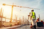 A man wearing a hardhat a rooftop construction site taking measurements