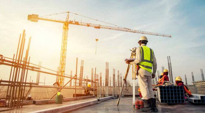 A man wearing a hardhat a rooftop construction site taking measurements