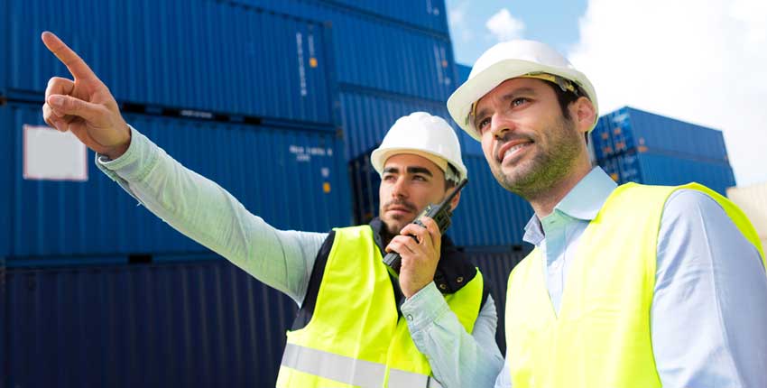 A transportation manager pointing to some shipping containers and talking into a radio